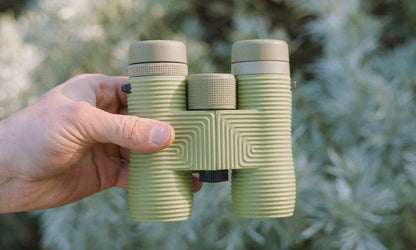 Hand holding a green binoculars against a blurred natural background