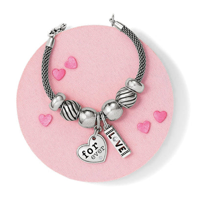 Brighton silver-plated beaded charm bracelet styled with heart and love charms on a pink background