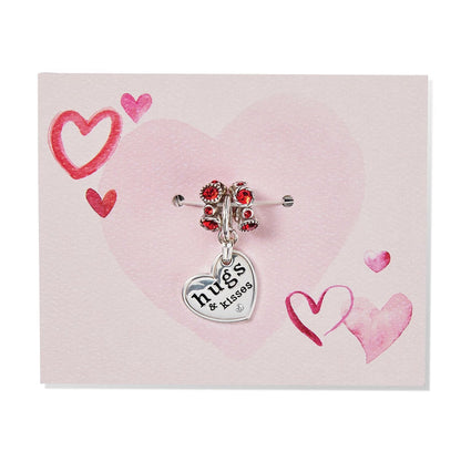 Brighton silver-plated heart charm with hugs and kisses engraving and red crystals styled on a pink heart card