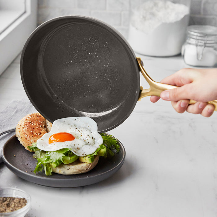 Ceramic nonstick frypan sliding a fried egg onto a bagel sandwich with avocado and lettuce.