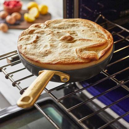Golden Dutch baby pancake in a cocoa-colored ceramic nonstick frypan with champagne handle on an oven rack.