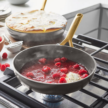 Ceramic nonstick frypan simmering raspberry sauce, with fresh raspberries and cream being added.