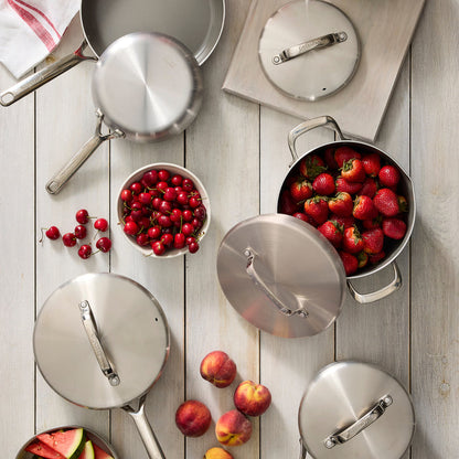 Stainless steel 10-piece cookware set with mirror handles on wood, next to strawberries, cherries, and peaches.