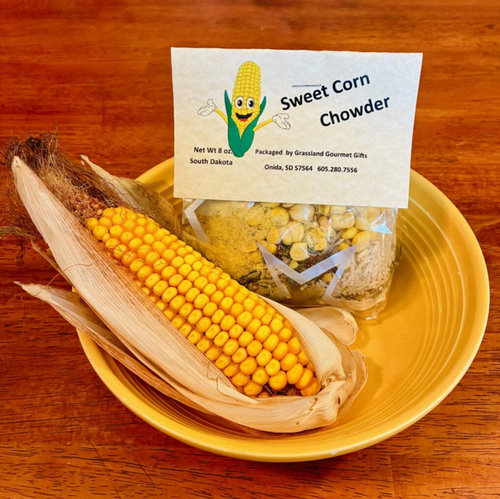 Corn on the cob and a package of Sweet Corn Chowder with a label on a wooden surface