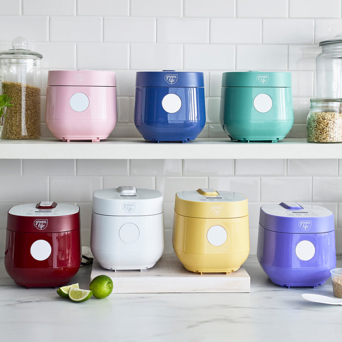 Blue GreenLife 4-cup rice and grains cooker on a white counter with glass jars of grains in the background.