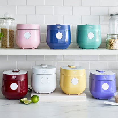 Blue GreenLife 4-cup rice and grains cooker on a white counter with glass jars of grains in the background.