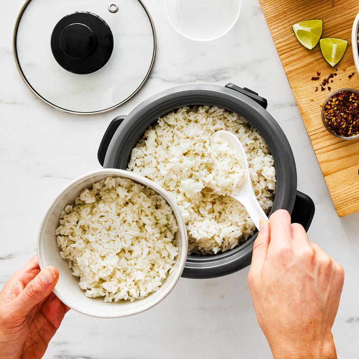 Hands spooning rice from a black GreenLife 6-cup rice cooker with ceramic coating into a white bowl.