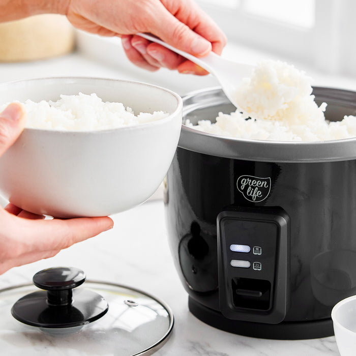 Cooked rice being spooned from a black GreenLife 6-Cup Rice Cooker into a white bowl.