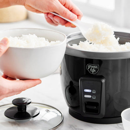 Cooked rice being spooned from a black GreenLife 6-Cup Rice Cooker into a white bowl.