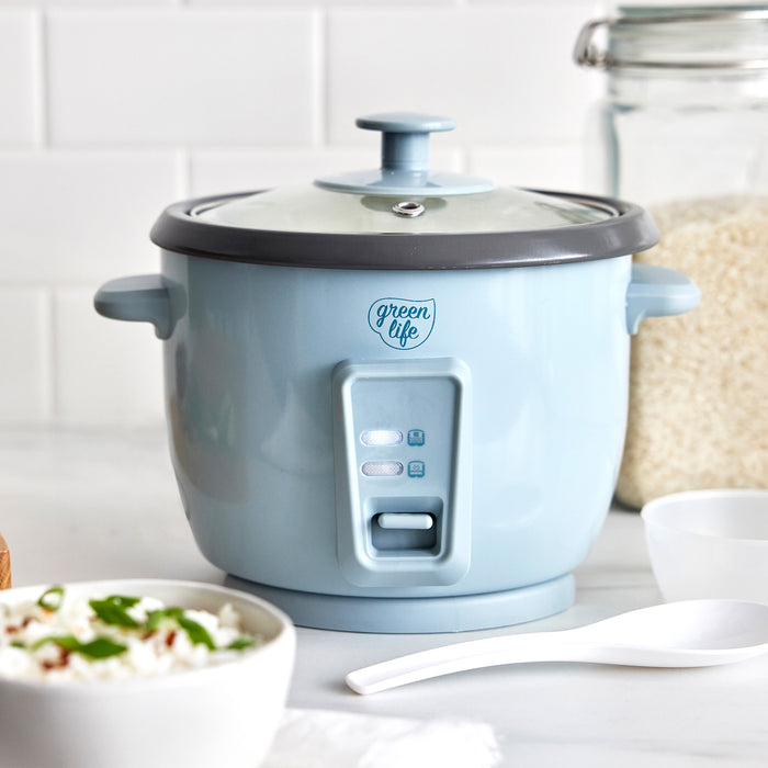 Blue GreenLife 6-cup rice cooker on a counter with a bowl of rice, white spoon, and jar of uncooked rice.
