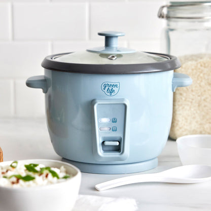 Blue GreenLife 6-cup rice cooker on a counter with a bowl of rice, white spoon, and jar of uncooked rice.