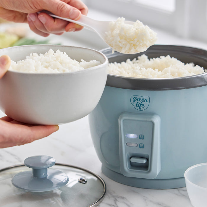 Cooked white rice being served from a blue GreenLife 6-cup rice cooker into a white bowl on a kitchen counter.