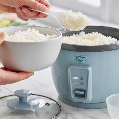Cooked white rice being served from a blue GreenLife 6-cup rice cooker into a white bowl on a kitchen counter.