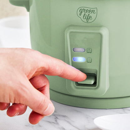 Hand pressing the switch on a sage green 6-cup rice cooker with ceramic nonstick pot and indicator lights.