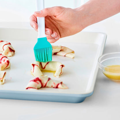 Brushing egg wash on crescent rolls arranged on a blue GreenLife ceramic nonstick baking sheet, 18x13.