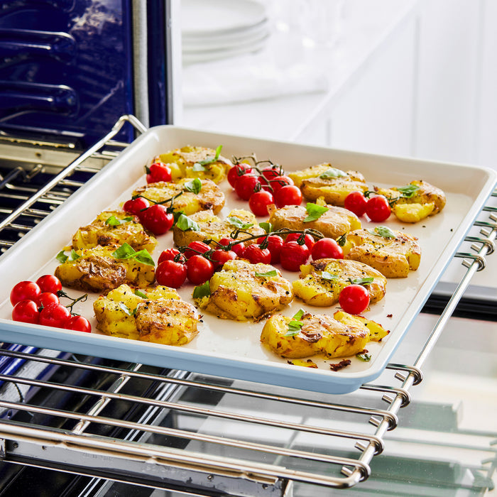 Smashed potatoes and cherry tomatoes with herbs on a GreenLife ceramic nonstick cookie sheet.