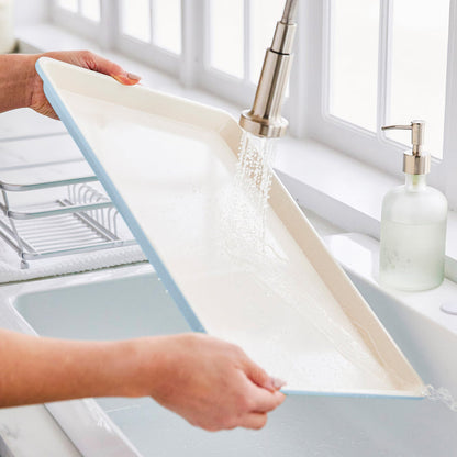 Blue GreenLife ceramic nonstick cookie sheet being rinsed under running water in a kitchen sink.