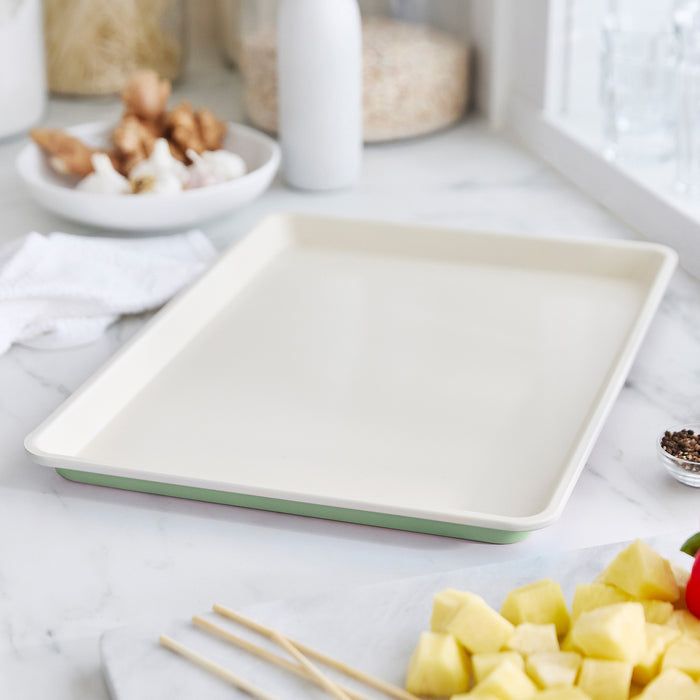 Sage green ceramic nonstick cookie sheet on a marble counter, vegetables visible nearby.