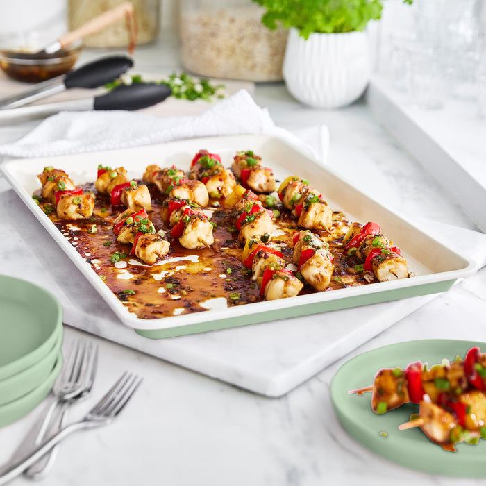 Chicken and vegetable skewers arranged on a sage green GreenLife ceramic nonstick baking sheet with herbs.