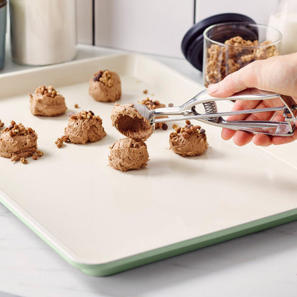 Hand placing chocolate cookie dough on a sage green ceramic nonstick cookie sheet.