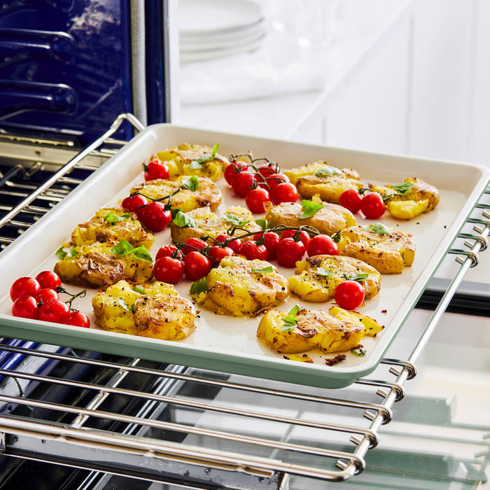 Oven-roasted smashed potatoes and tomatoes on a large GreenLife ceramic cookie sheet with a blue rim.