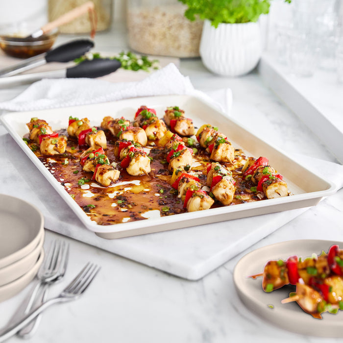 Taupe ceramic cookie sheet with chicken and veggie skewers, shown on a counter.