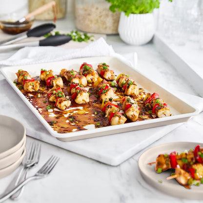 Taupe ceramic cookie sheet with chicken and veggie skewers, shown on a counter.