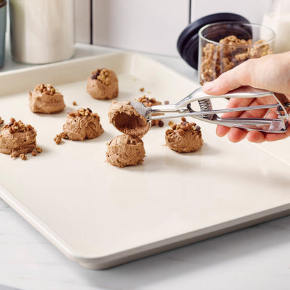 Hand scooping cookie dough onto a taupe ceramic nonstick baking sheet.