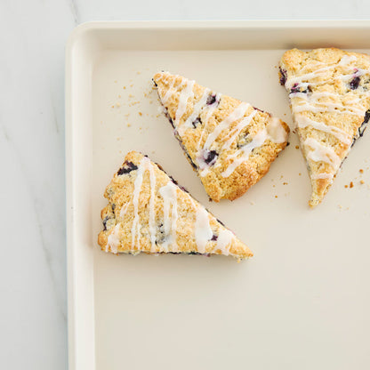 Three blueberry scones with white icing on a taupe GreenLife ceramic cookie sheet, 18 x 13 inches.