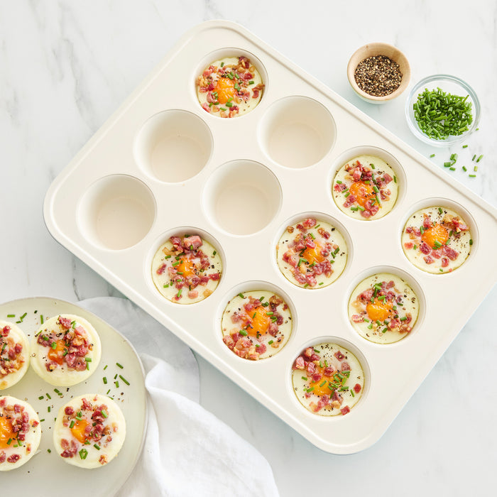 Six egg bites with ham, cheese, and chives in a blue GreenLife muffin pan on a white countertop.