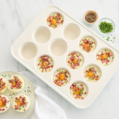 Six egg bites with ham, cheese, and chives in a blue GreenLife muffin pan on a white countertop.