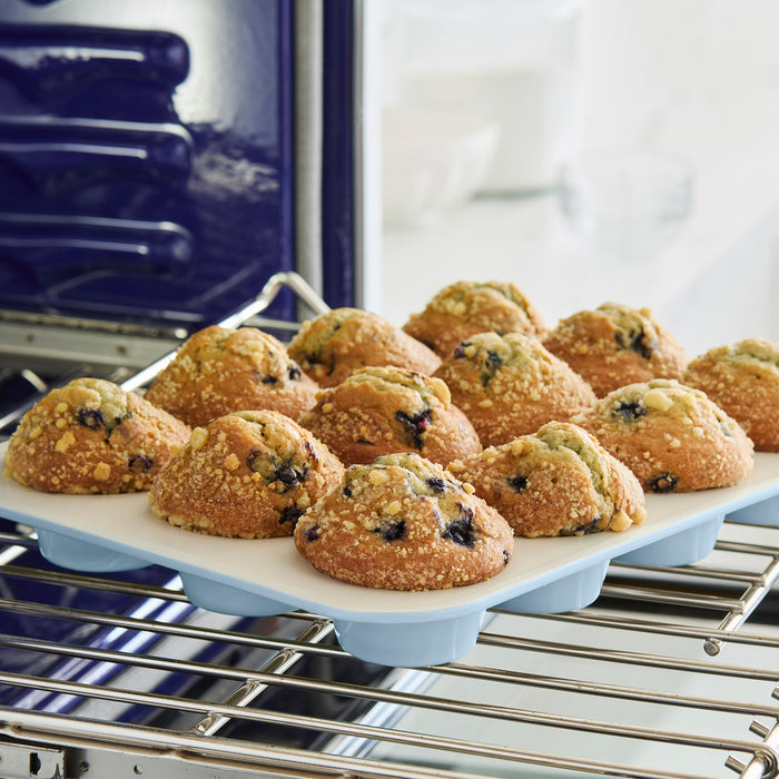 Blue ceramic nonstick muffin pan with a set of fresh blueberry muffins on an oven rack.