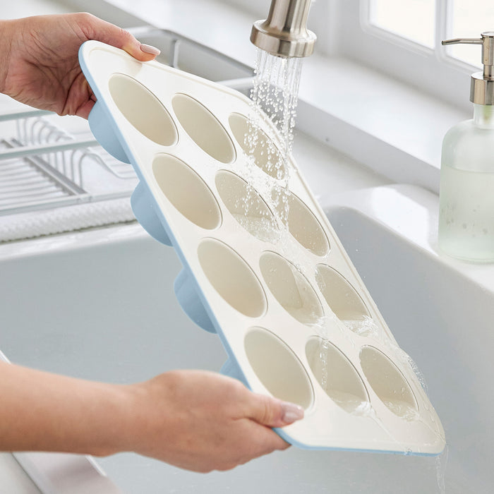 Washing a blue GreenLife ceramic muffin pan under running water in a kitchen sink.