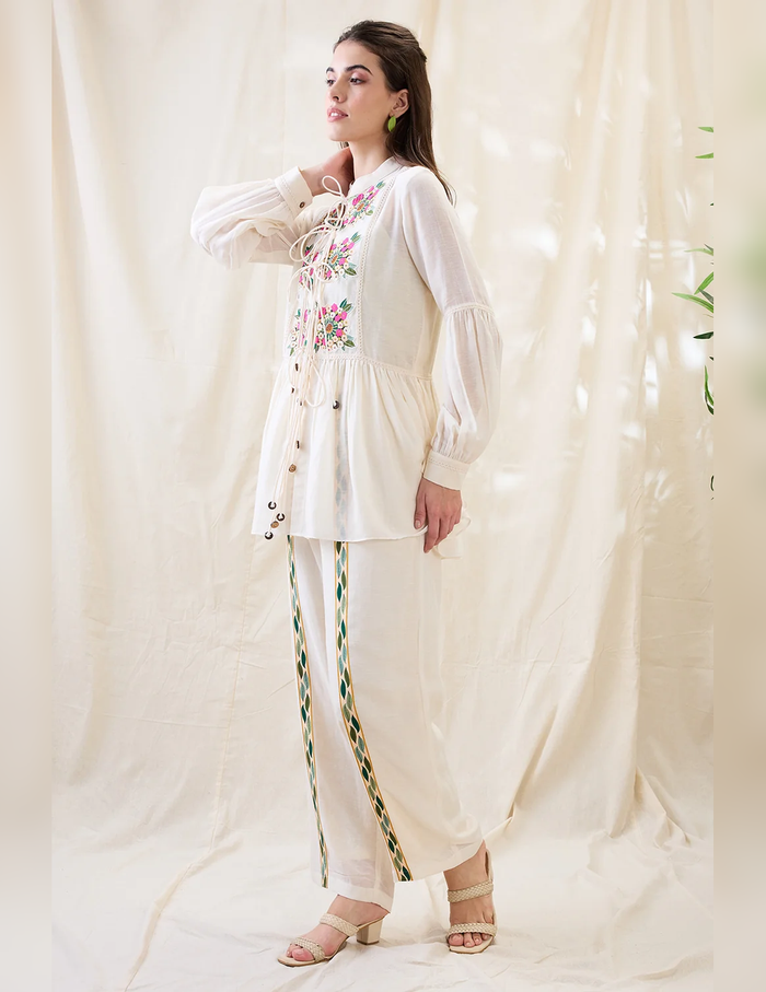 White Gulzaar Appliquéd Peplum Top with front tie-ups paired with straight linen pants, offering an elegant and refined contemporary silhouette.