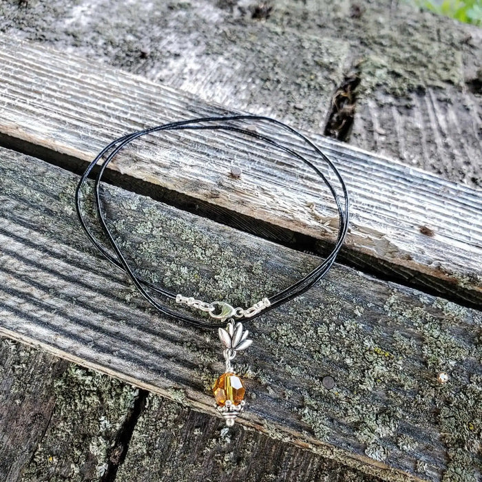 Handmade silver crystal pineapple leather necklace with yellow Austrian Swarovski crystal on a wooden background.