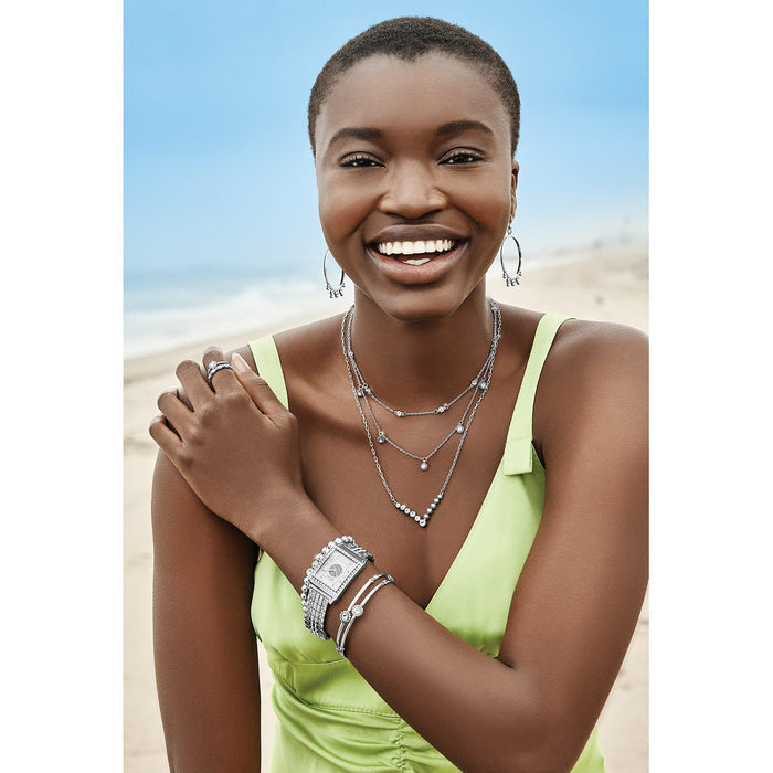 Model wearing Brighton silver hoop earrings with layered crystal necklaces, watch, bangles, and crystal ring