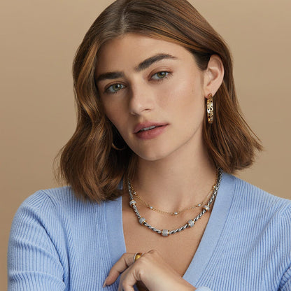 Model wearing Brighton gold-plated hoop earrings paired with layered silver and gold necklaces with crystal accents