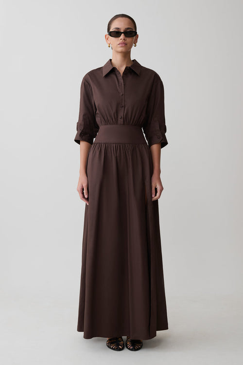 Woman wearing a long brown dress with a belt on a white background