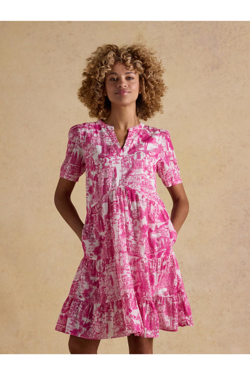 Model wearing Joules H63479 Ariella Pink Toile Tiered Dress with short sleeves and V-neck, featuring a pink toile pattern by Joules. Shop Joules at Dotique.
