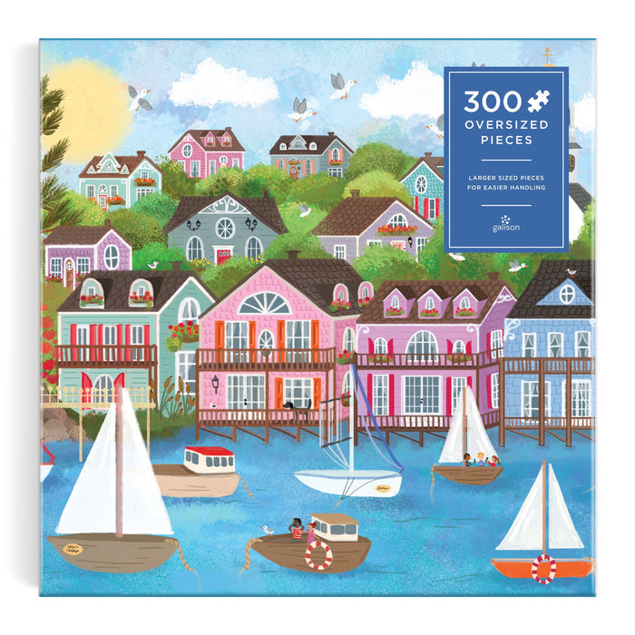 The Joy Laforme Harbor by the Sea 300 Piece Puzzle features colorful coastal houses, boats on blue water, and a bright sky. Oversized pieces make this Joy Laforme puzzle easy to handle.