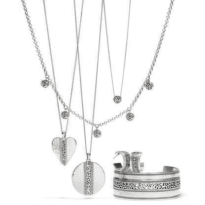 Brighton silver-plated jewelry set styled with layered scroll pendant necklaces, hoop earrings, and engraved cuff bracelet on white background