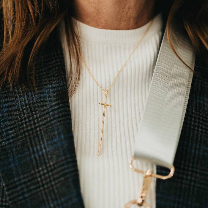 Person wearing a gold cross necklace with a blurred background