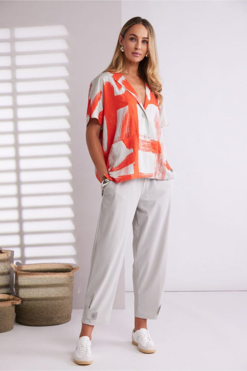 Model wearing Naya NPA26179 Slim Leg Trouser With Tab At Hem Ash paired with an orange abstract print blouse, shop Naya at Dotique.
