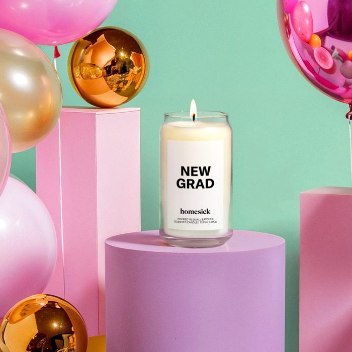 A lifestyle image of the New Grad Homesick candle with various celebratory surrounding it.