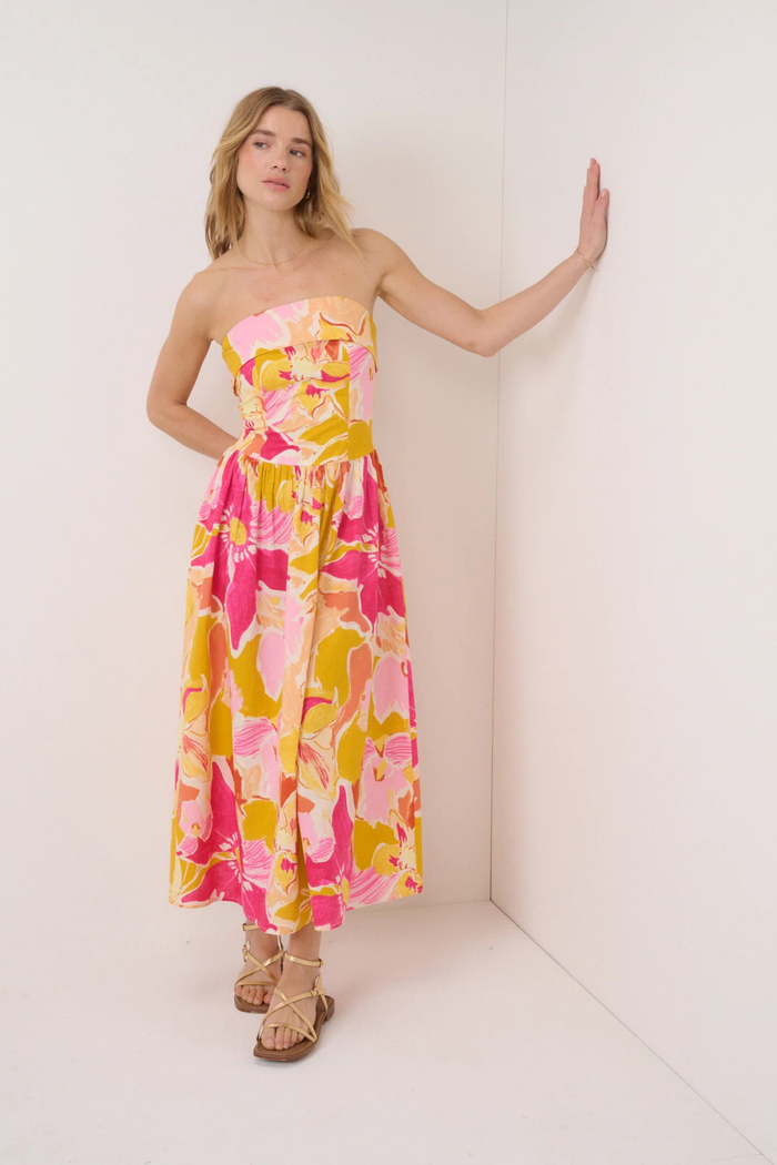 Model wearing Nobody's Child Pink Floral Fia Linen Midi Dress with strapless design and vibrant pink, yellow, and peach floral print by Nobody’s Child. Shop Nobody’s Child at Dotique.