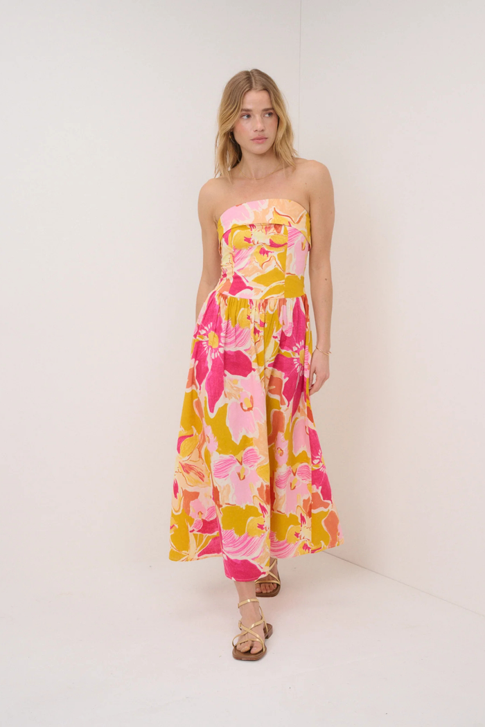 Model wearing Nobody's Child Pink Floral Fia Linen Midi Dress with strapless bodice and vibrant floral print by Nobody’s Child. Shop Nobody’s Child at Dotique.
