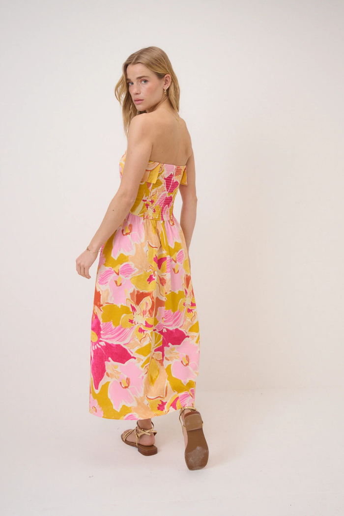 Model showcasing Nobody's Child Pink Floral Fia Linen Midi Dress with strapless design and vibrant pink, yellow, and orange floral print by Nobody’s Child. Shop Nobody’s Child at Dotique.