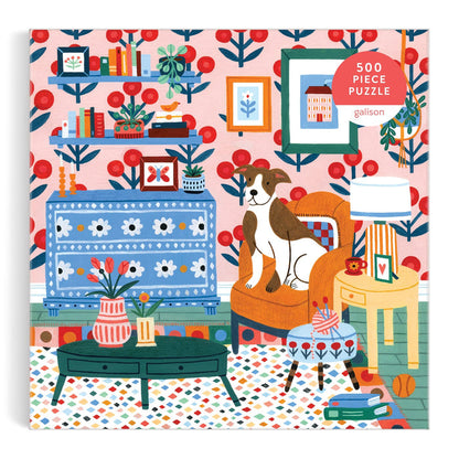 Pattern & Petal 500 Piece Puzzle by Molly Egan features a vibrant living room scene with patterned wallpaper, bookshelves, a blue table, flower vases, an orange armchair with a dog, and playful decor.