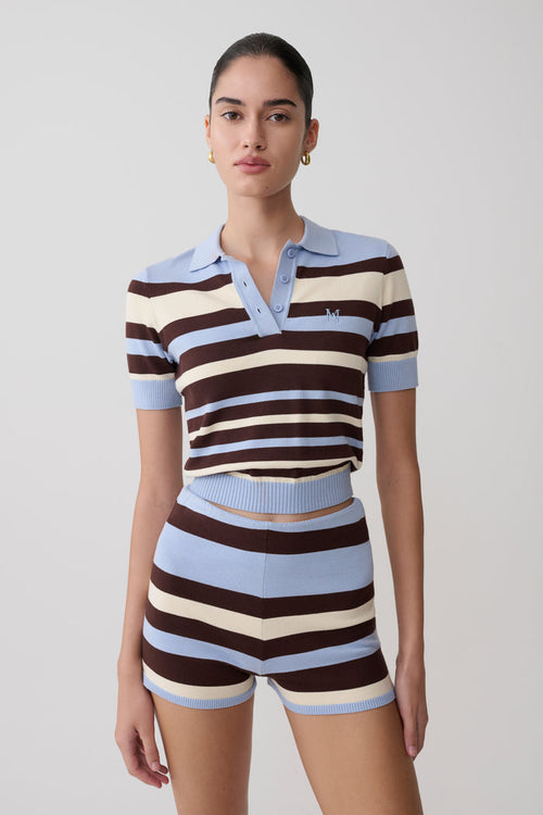 Woman wearing a striped polo shirt and shorts on a plain background.