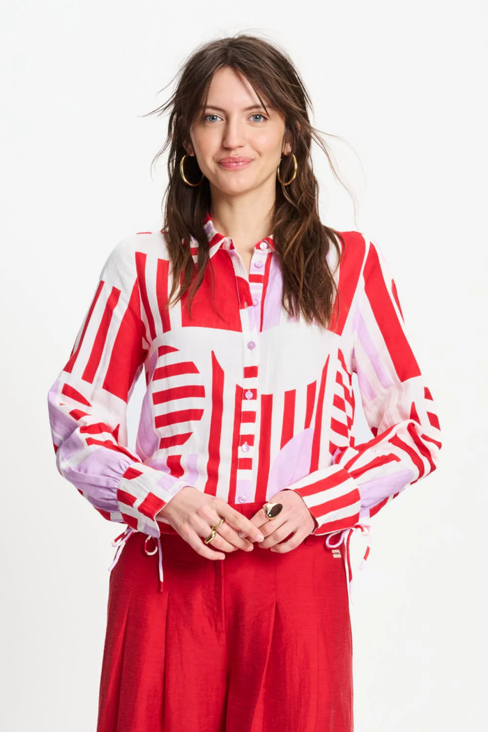 Model wearing Pom Amsterdam SP9584 Sundeck Linen Blouse with bold red and pink geometric print, styled with red pants. Shop Pom Amsterdam at Dotique.